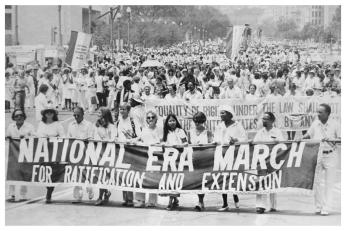 A group of demonstrators march with a large banner reading "National ERA March for Ratification and Extension" in their hands