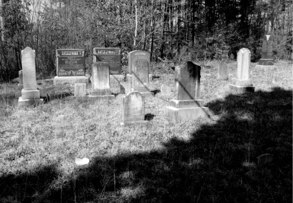 A black and white photograph of a cemetery. About ten medium-sized tombstones are visible.