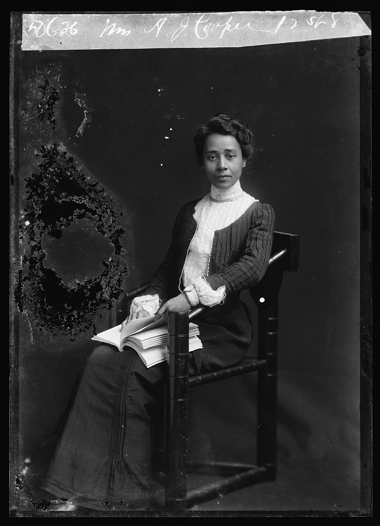Educator-Writer Anna Julia Cooper photographed seated with book in hand and dressed in white collared black gown