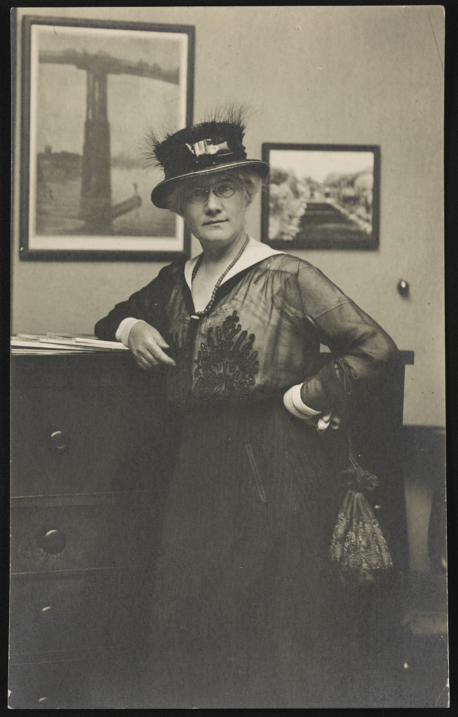 Portrait of Mattie Hewitt leaning against a dresser in a bedroom. 