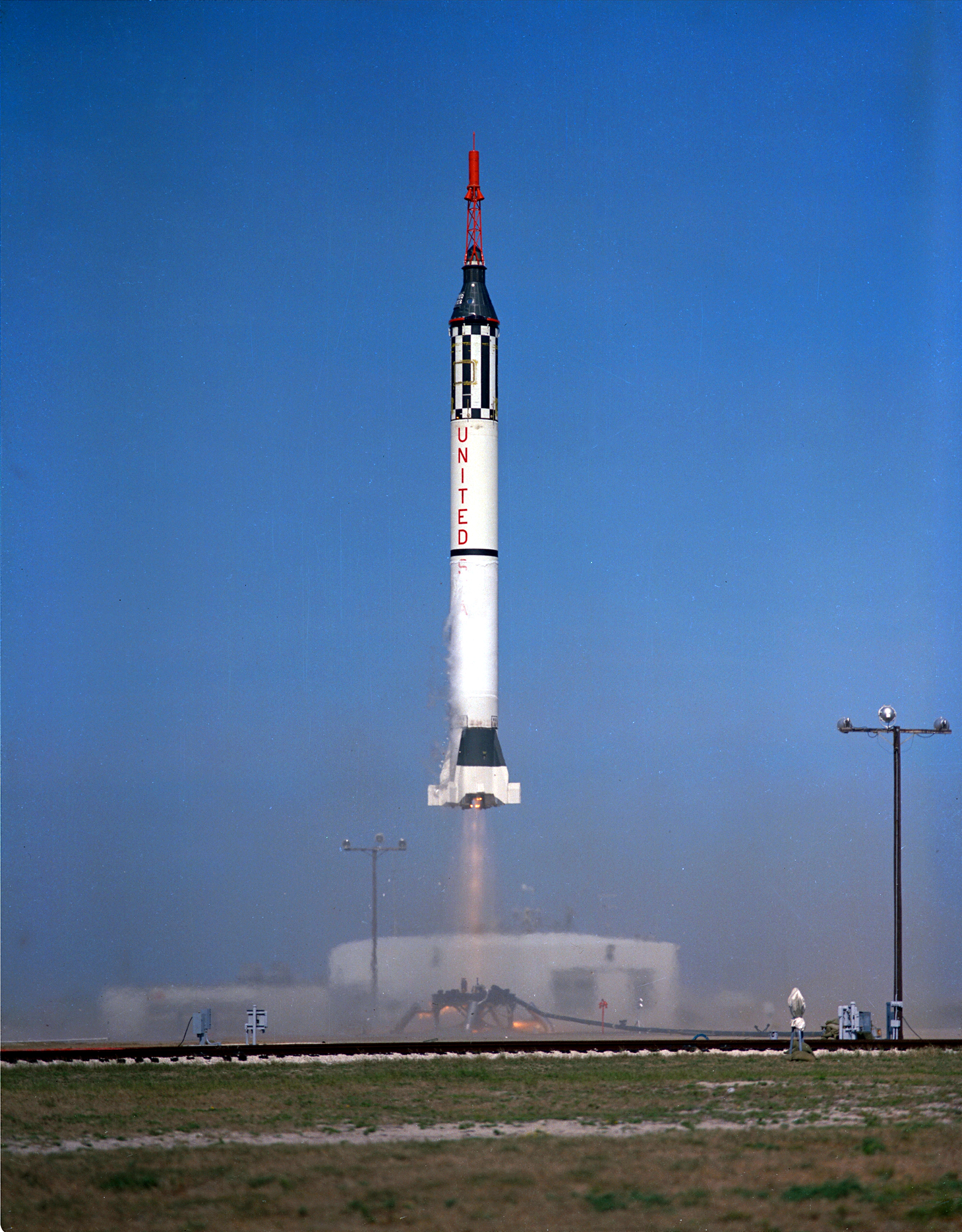 Color photo of NASA rocket lifting off from launch pad on with clear blue skies.