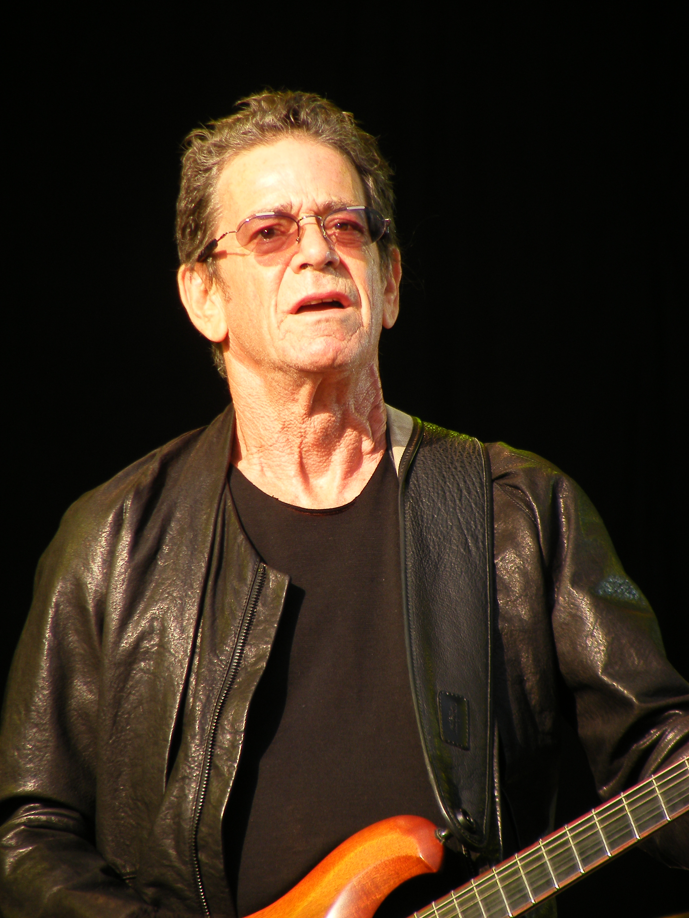 White man with glasses playing guitar. 