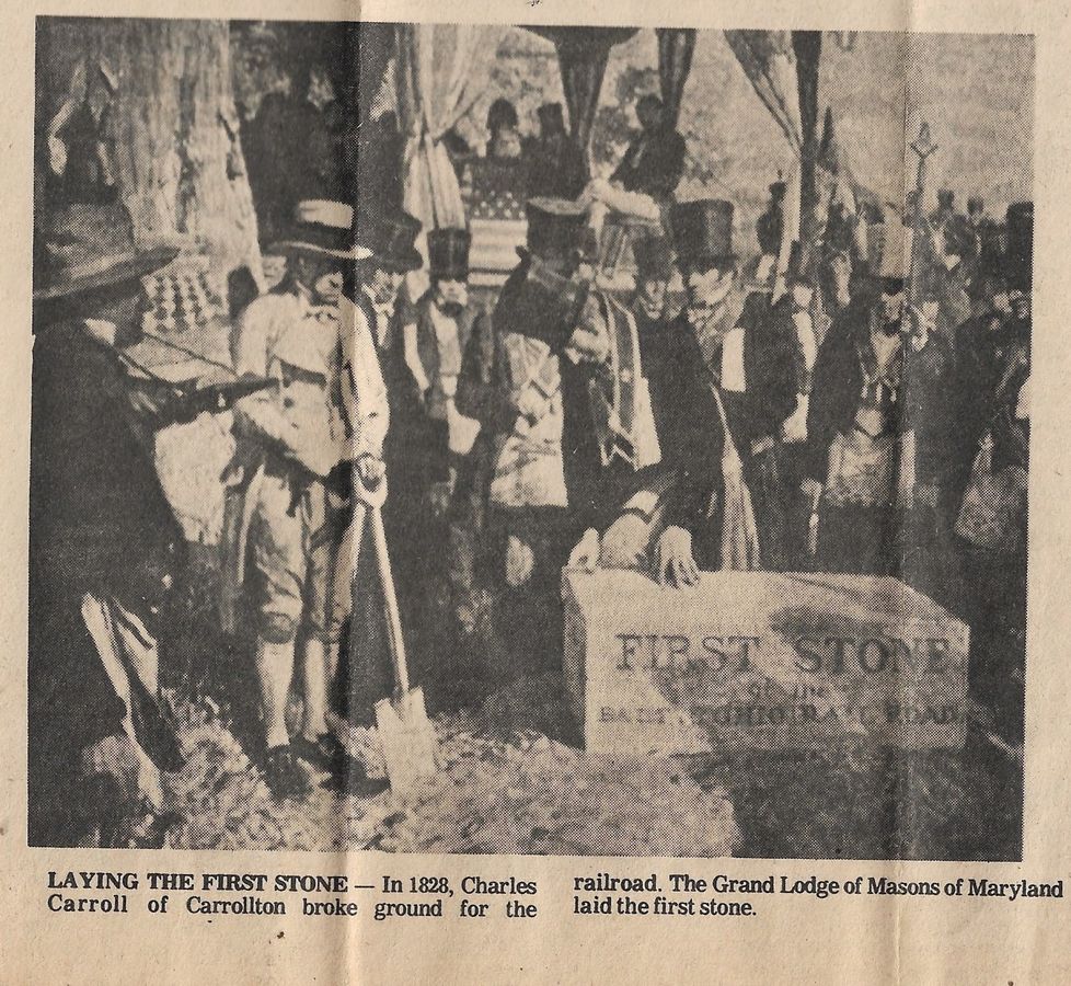 A historical scene with men in 19th-century attire at a ceremonial stone-laying event.  Transcribed Text:  LAYING THE FIRST STONE — In 1828, Charles Carroll of Carrollton broke ground for the railroad. The Grand Lodge of Masons of Maryland laid the first stone. FIRST STONE BALTIMORE AND OHIO RAIL ROAD