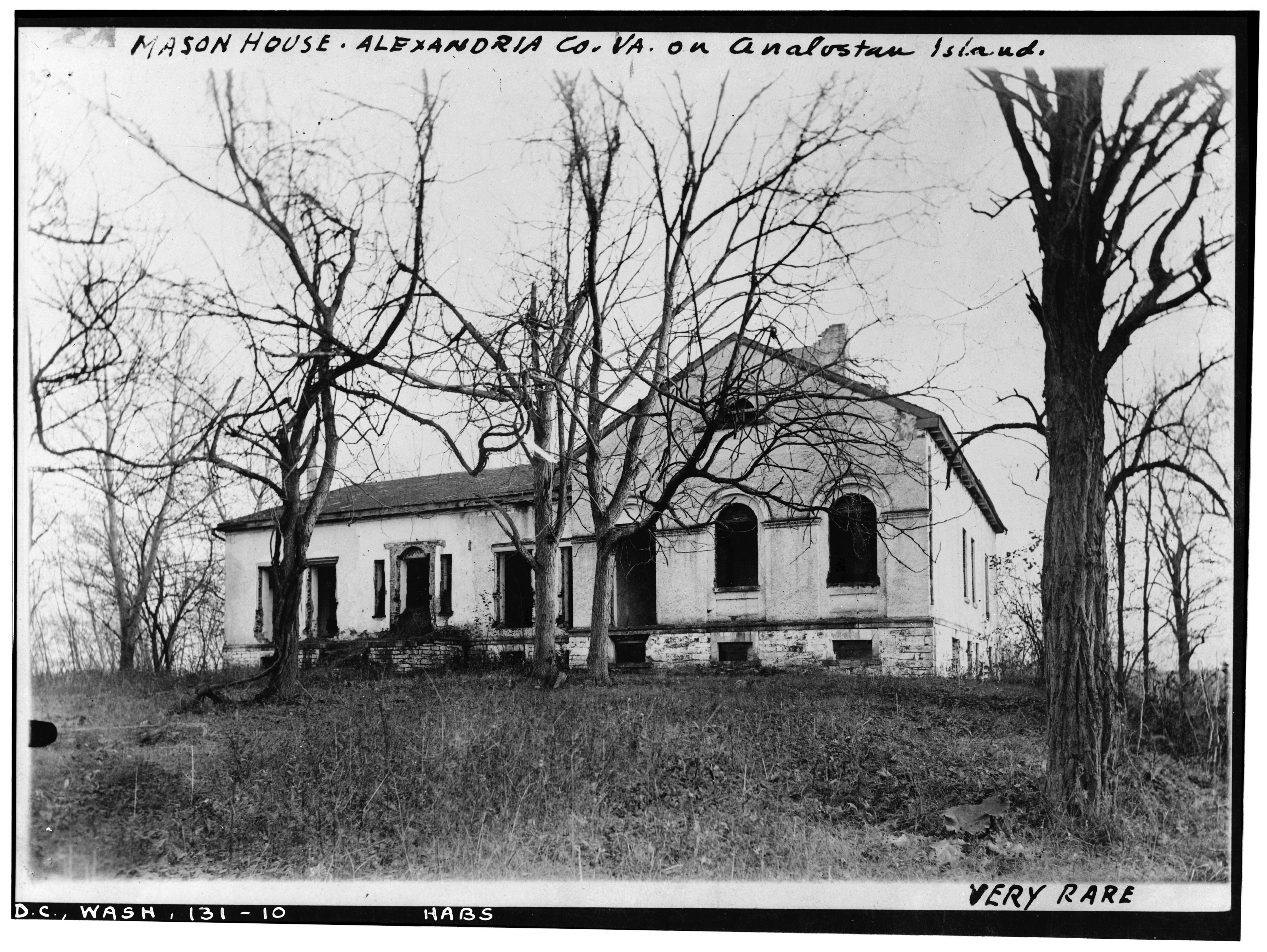 Old white house on hilltop. Trees without leaves stand in front of the house.