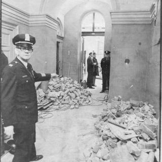 Capitol Police officer stands in a damaged hallway with rubble visible.