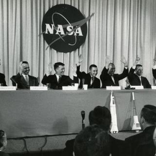 “The Mercury 7 astronauts (left to right) Slayton, Shepard, Schirra, Grissom, Glenn, Cooper, and Carpenter all raise their hands in reply to a question about whether they felt confident they would return from space – Glenn raised both hands,” 1959 (Photo Source: NASA) https://www.nasa.gov/feature/60-years-ago-nasa-introduces-mercury-7-astronauts