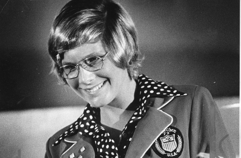 Melissa Belote holding gold medal and wearing Olympic jacket.