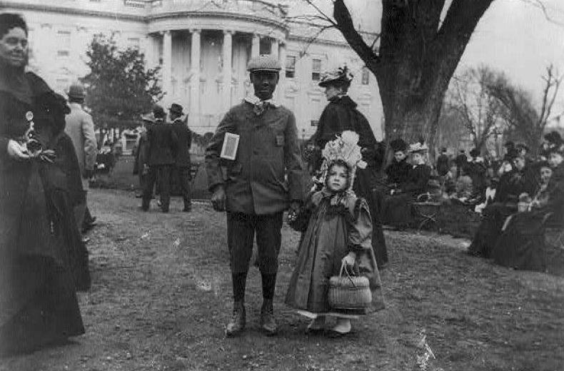 African American boy holding hand of small white girl during Easter egg roll