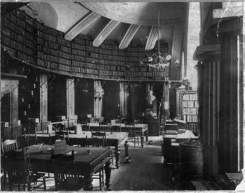 Fine wooden tables sit in the law library of the Supreme Court. Overhead book shelves line the rounded walls.