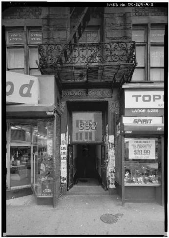 Black-and-white photo of the exterior of the 9:30 Club, a door between two storefronts with 9:30 printed on the front and a fire escape above