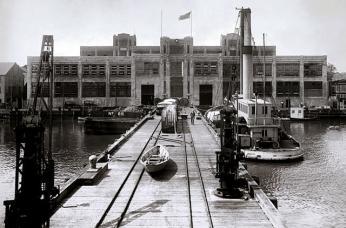 A black-and-white photo of the torpedo factory, a large building at the end of a pier
