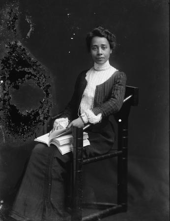 A black-and-white photograph of Anna Julia Cooper seated in a photo studio with a book on her lap