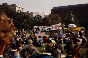 Photo of protestors sitting in city square holding "End the War Now" banner.