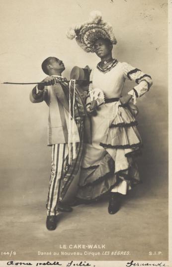 Two black actors, Gregory and Brown, one in drag, dancing the Cake-Walk in Paris. Photographic postcard, 1903