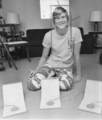 Melissa Belote sits on the floor at home with three gold medals on the floor in front of her.