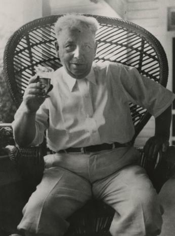 An older man holds up a drink to the camera.