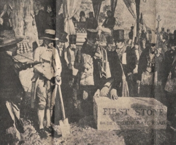 A historical scene with men in 19th-century attire at a ceremonial stone-laying event.  Transcribed Text:  LAYING THE FIRST STONE — In 1828, Charles Carroll of Carrollton broke ground for the railroad. The Grand Lodge of Masons of Maryland laid the first stone. FIRST STONE BALTIMORE AND OHIO RAIL ROAD