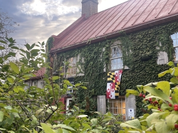 Stone house with ivy growing on the walls and a Maryland flag hanging from window.