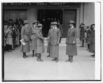 First Lady Grace Coolidge shakes the hand of Leona Baldwin in front of the Tivoli Theater. Both women are wearing wide-brimmed hats with long blazers and skirts.