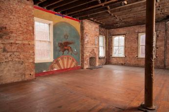 The mural is adjacent to a part of the floor that was removed to create a women’s balcony when 415 M was a synagogue. Although the floor boards were subsequently replaced, the visible incongruity indicates the outline of the earlier hole between the first and second floors. Patricia Fisher, Fisher Photography, 2014.