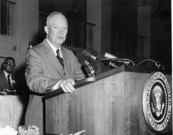 President Dwight Eisenhower standing at a podium, wearing a nice suit and speaking to a crowd.
