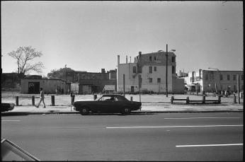 14th Street lays bare after the 1968 riots. A solitary car sits in front of an empty lot with dilapidated buildings behind it.