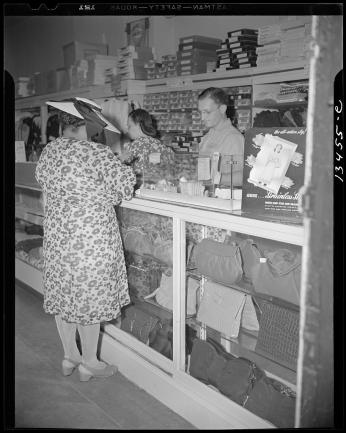 Female shopper standing at a counter with a man and woman behind it. It looks like she is paying for her goods. 