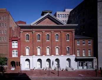 Exterior of Ford's Theatre, ca. 1980-2006 A color photo of the exterior of Fords Theatre and surrounding buildings ca. 1980-2006. The building is three stories, red brick, with tall windows across every floor. The roof is pointed.