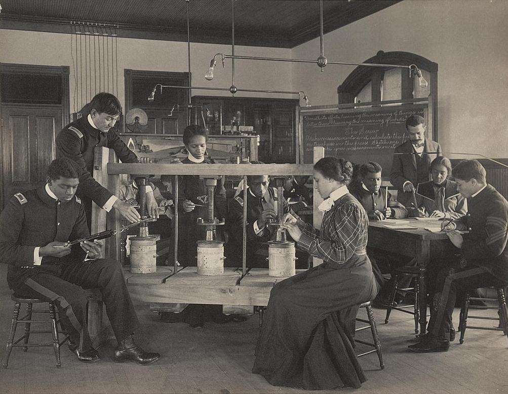 Young men and women students operating a cheese press in a classroom.