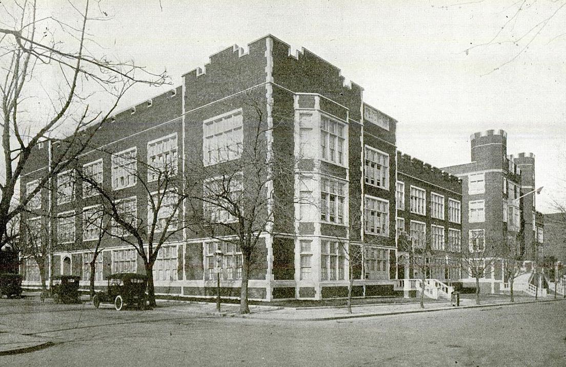 Streetview image of Dunbar High School circa 1917. Castle-like red brick and stone trimmed structure with cars parked on left side.