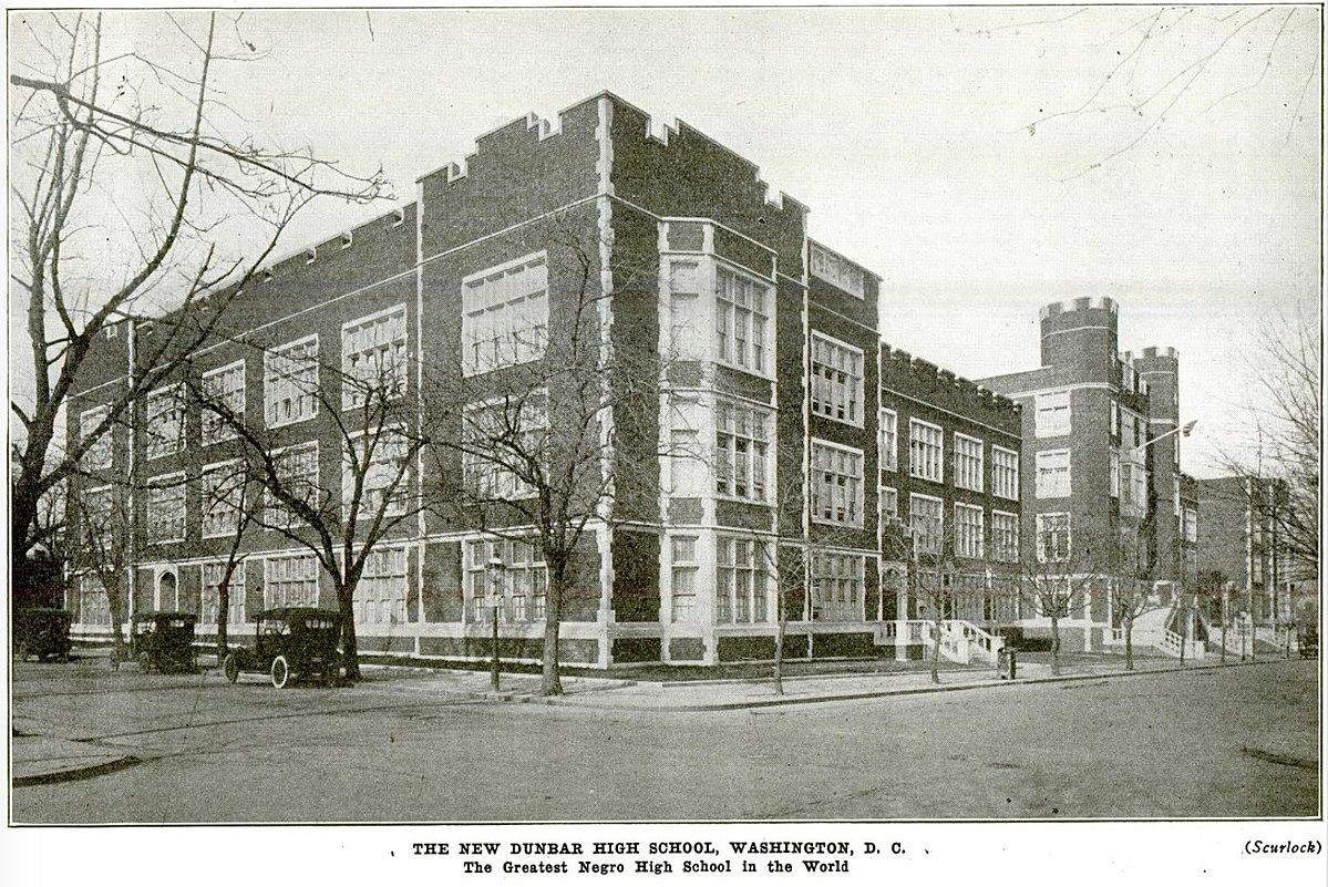 Streetview image of Dunbar High School circa 1917. Castle-like red brick and stone trimmed structure with cars parked on left side.