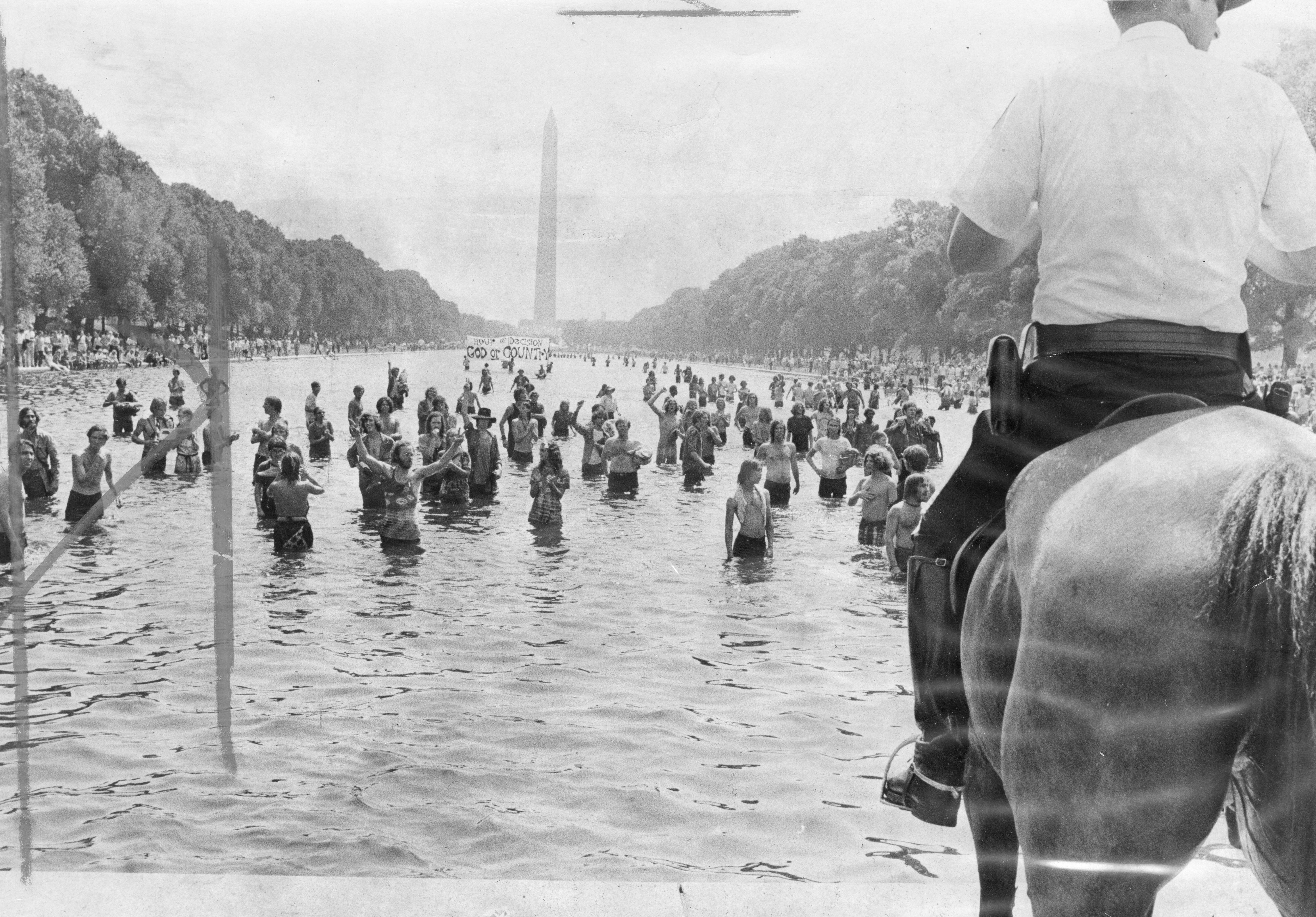 A police officer on horseback overlooks Hippies wading in the Reflection Pool on Honor America Day.