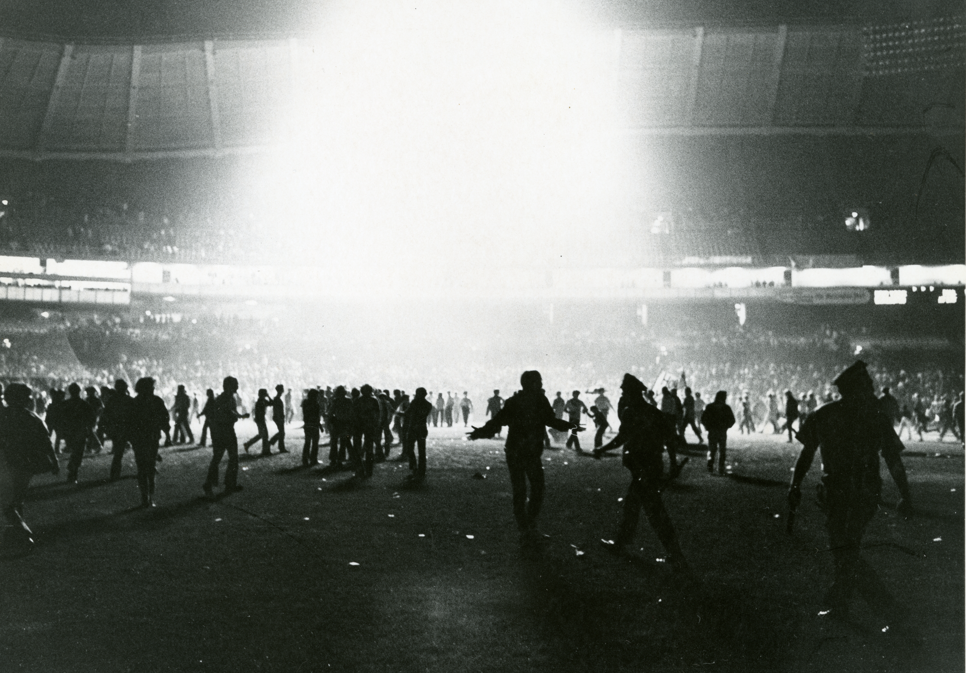 Light shines down from the roof of the Senators baseball stadium, illuminating hundreds of fans storming the field.