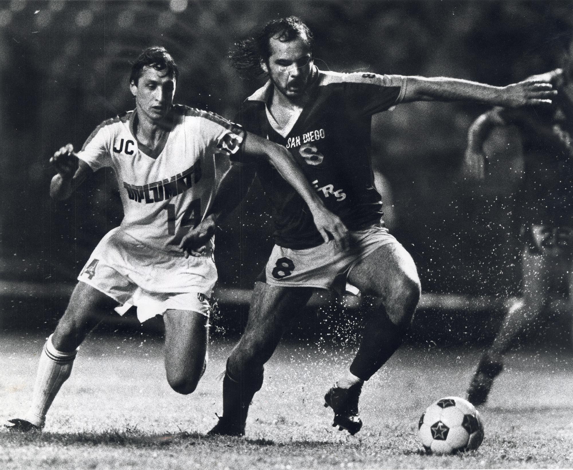 Two soccer players run after ball in rain. [Reprinted with permission of the DC Public Library, Star Collection, © Washington Post]