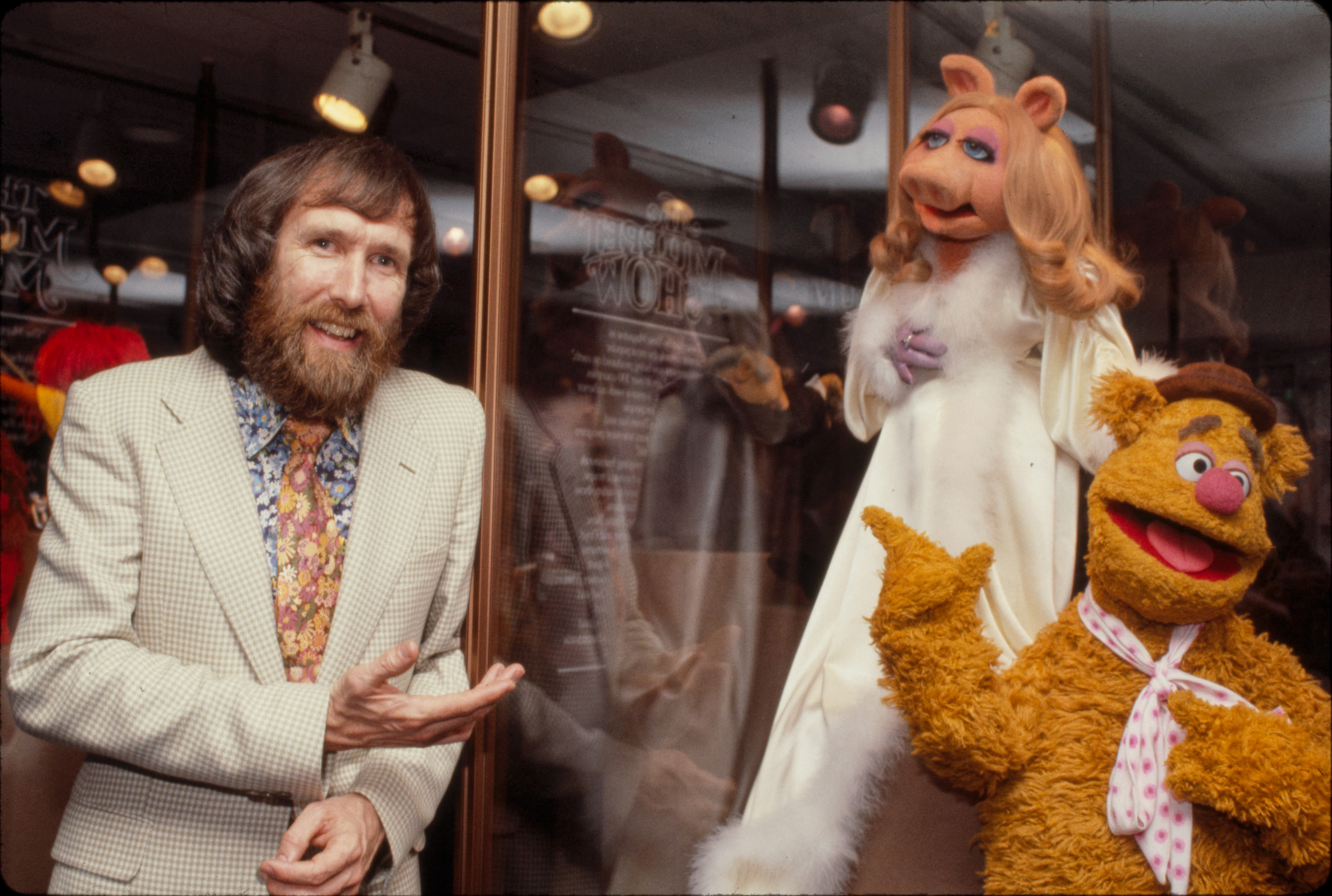 Jim Henson dressed in white suit standing with Miss Piggy and Fozzie Bear