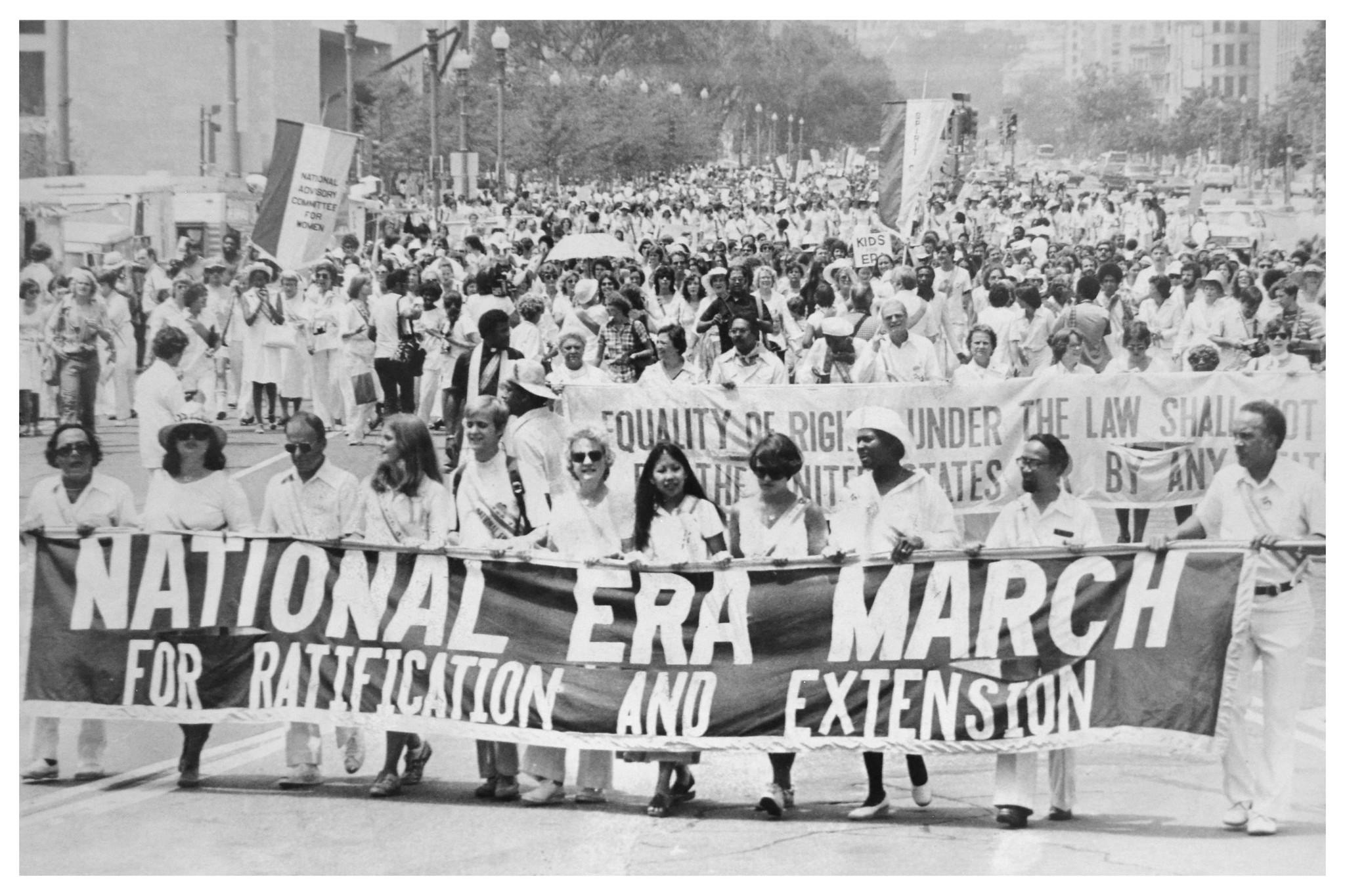 A group of demonstrators march with a large banner reading "National ERA March for Ratification and Extension" in their hands