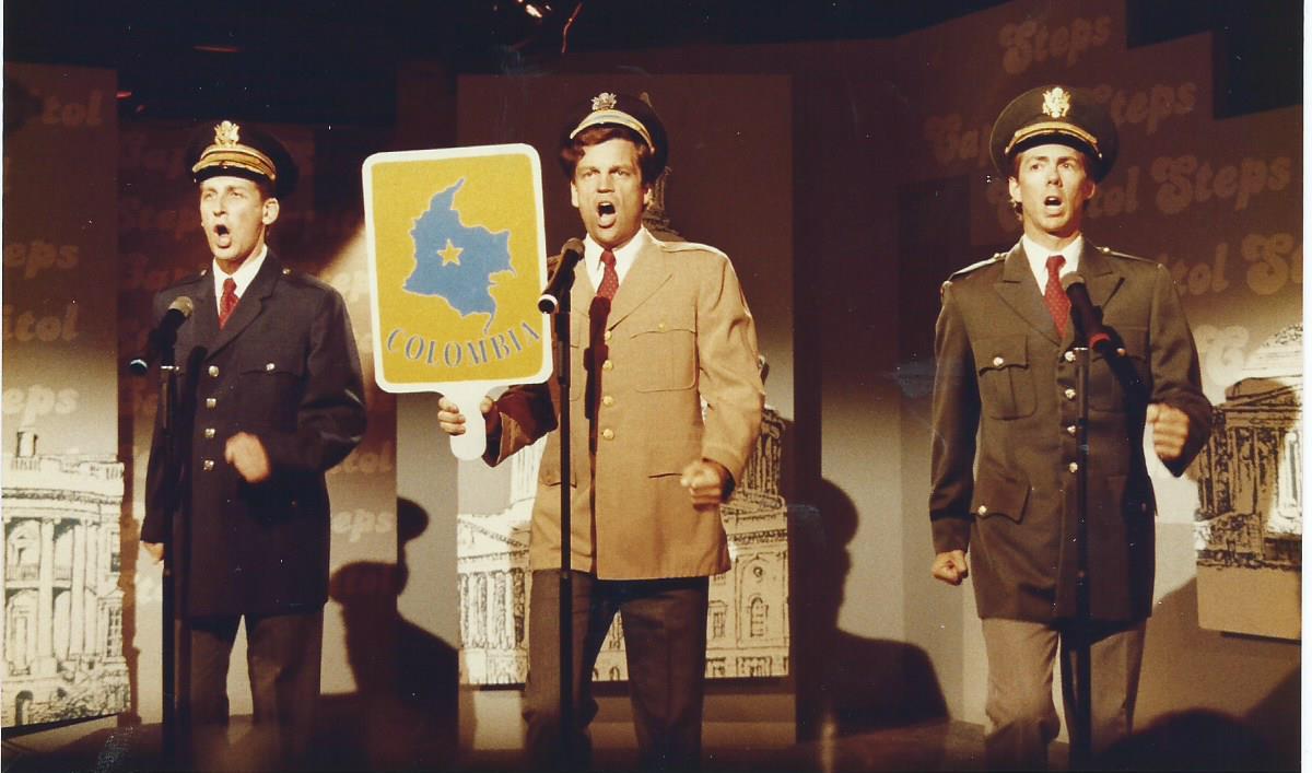 Three men performing on stage at WETA with a sign that says "Columbia".